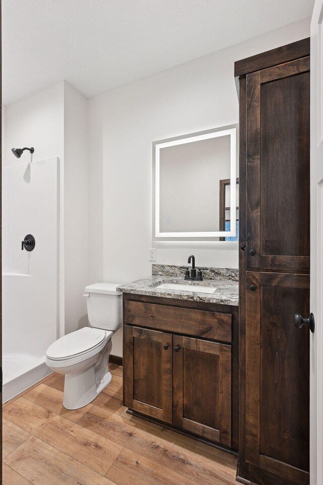 bathroom featuring a shower, wood-type flooring, vanity, and toilet