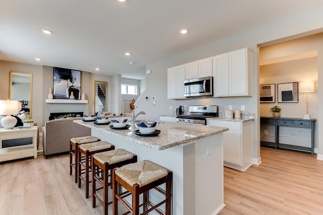 kitchen with sink, stainless steel appliances, light hardwood / wood-style flooring, a center island with sink, and white cabinets