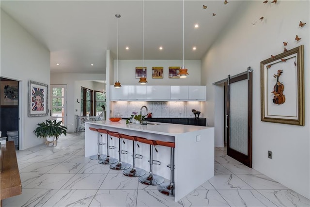 kitchen with white cabinetry, a barn door, backsplash, decorative light fixtures, and a kitchen bar