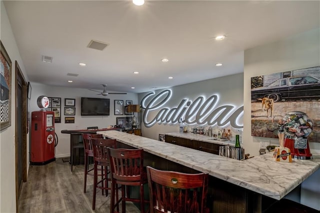 bar with light stone countertops, light hardwood / wood-style floors, and ceiling fan