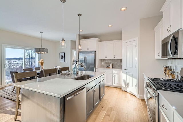 kitchen featuring sink, white cabinetry, hanging light fixtures, appliances with stainless steel finishes, and an island with sink