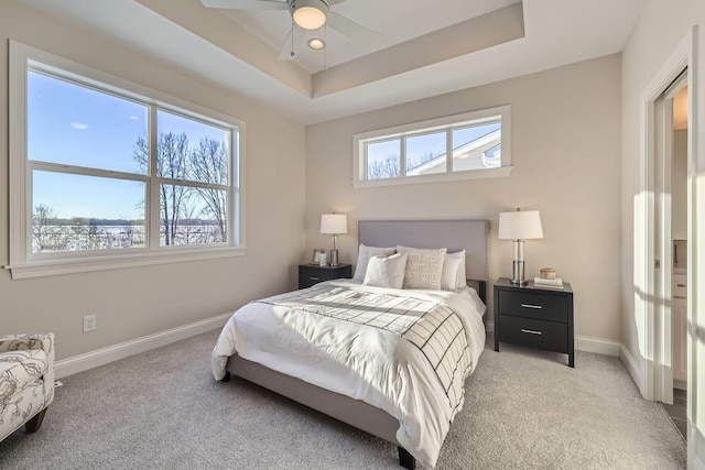 bedroom featuring multiple windows, light colored carpet, a raised ceiling, and ceiling fan