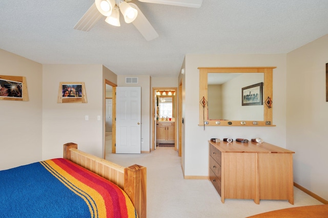 bedroom featuring ceiling fan, light colored carpet, a textured ceiling, and ensuite bath