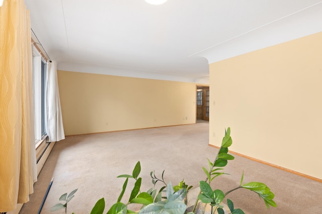 spare room with baseboard heating, light colored carpet, and a healthy amount of sunlight