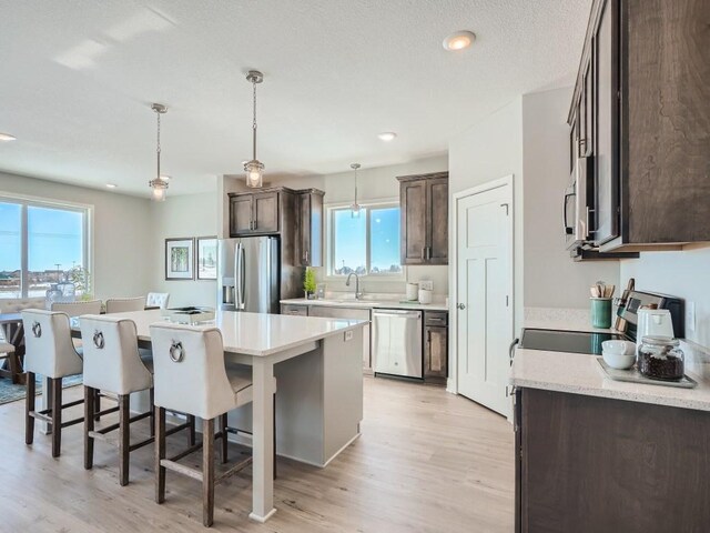 kitchen featuring a center island, sink, hanging light fixtures, light wood-type flooring, and stainless steel appliances