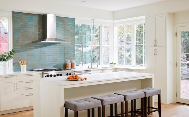 kitchen with decorative light fixtures, white cabinetry, light hardwood / wood-style floors, backsplash, and wall chimney range hood