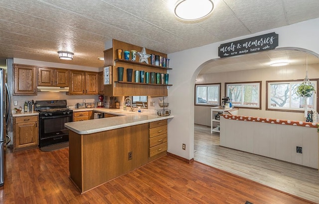 kitchen featuring kitchen peninsula, black gas range oven, dark hardwood / wood-style floors, and sink