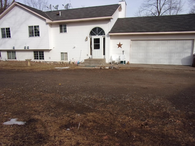 view of front of home with a chimney, a garage, and dirt driveway