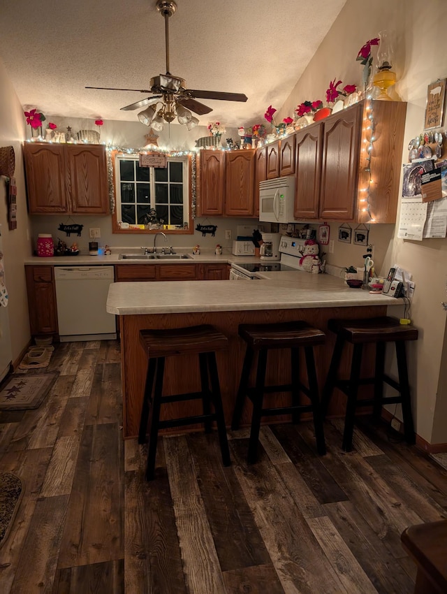 kitchen featuring dark wood-type flooring, light countertops, a peninsula, white appliances, and a sink