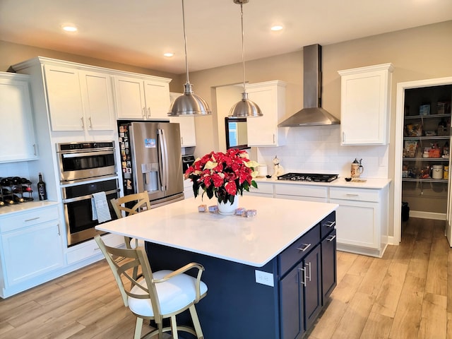 kitchen with wall chimney range hood, backsplash, decorative light fixtures, white cabinets, and appliances with stainless steel finishes