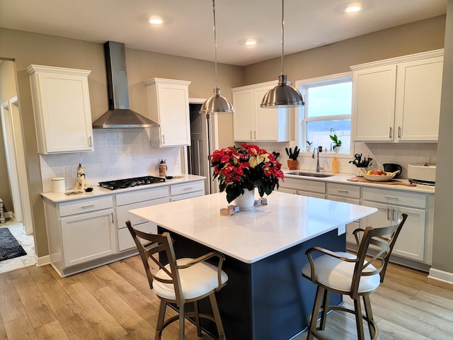 kitchen with white cabinets, wall chimney exhaust hood, a kitchen island, a kitchen bar, and stainless steel gas cooktop