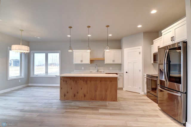 kitchen with white cabinetry, sink, stainless steel appliances, an island with sink, and decorative light fixtures