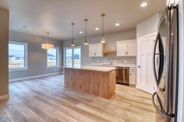 kitchen featuring white cabinetry, sink, a center island, hanging light fixtures, and appliances with stainless steel finishes