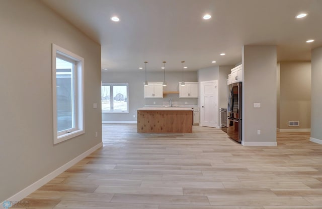 kitchen featuring white cabinets, stainless steel fridge, an island with sink, decorative light fixtures, and light hardwood / wood-style floors