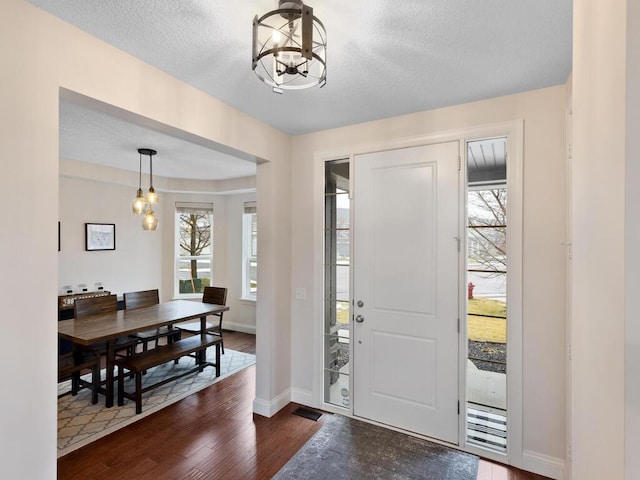 foyer with dark wood-type flooring, a wealth of natural light, and an inviting chandelier