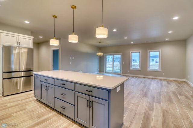 kitchen featuring light wood-type flooring, gray cabinets, stainless steel refrigerator, and hanging light fixtures