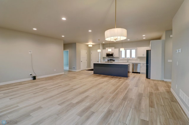 kitchen featuring appliances with stainless steel finishes, a kitchen island, decorative light fixtures, light hardwood / wood-style floors, and white cabinetry