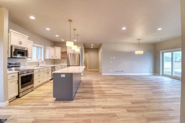 kitchen featuring white cabinetry, a center island, sink, stainless steel appliances, and pendant lighting