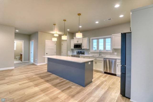 kitchen with a center island, sink, hanging light fixtures, white cabinetry, and stainless steel appliances