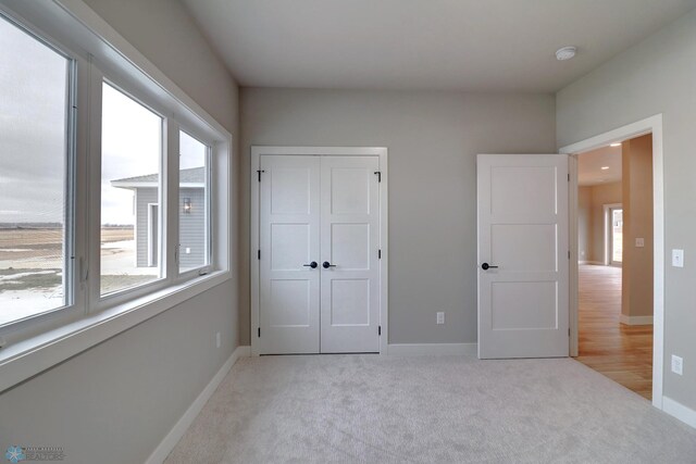 unfurnished bedroom featuring light colored carpet, multiple windows, and a closet