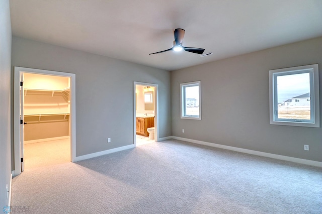 unfurnished bedroom with a walk in closet, ceiling fan, connected bathroom, light colored carpet, and a closet