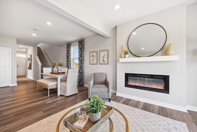 living room featuring a glass covered fireplace, stairway, baseboards, and wood finished floors