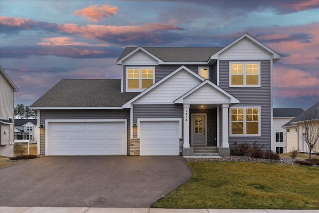 view of front facade featuring stone siding, an attached garage, a shingled roof, a yard, and aphalt driveway