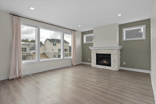 unfurnished living room with a fireplace, light wood-style floors, visible vents, and baseboards