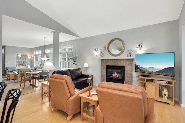 living room featuring ornate columns, a tile fireplace, vaulted ceiling, and light wood-type flooring