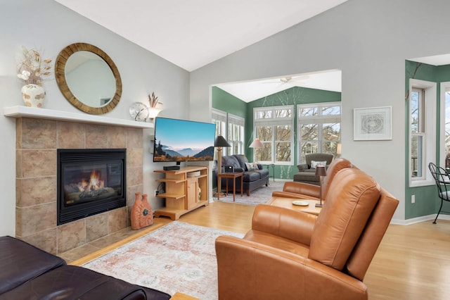 living room with ceiling fan, lofted ceiling, a tile fireplace, and light hardwood / wood-style flooring