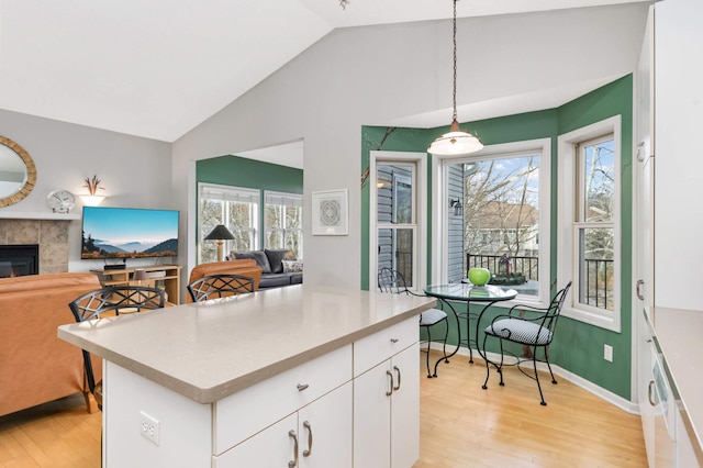 kitchen with pendant lighting, a fireplace, white cabinetry, lofted ceiling, and light hardwood / wood-style flooring