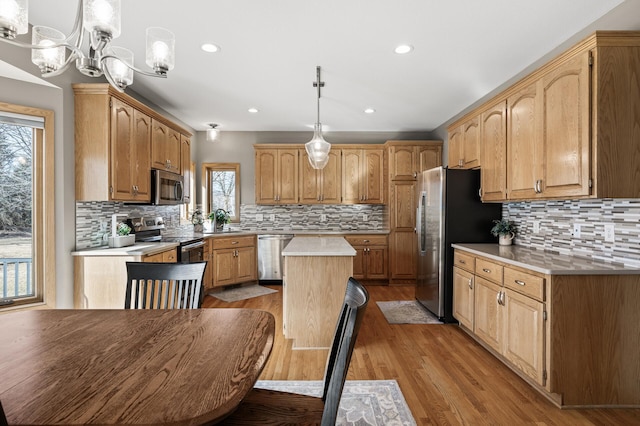 kitchen featuring backsplash, a kitchen island, light countertops, appliances with stainless steel finishes, and light wood-style floors