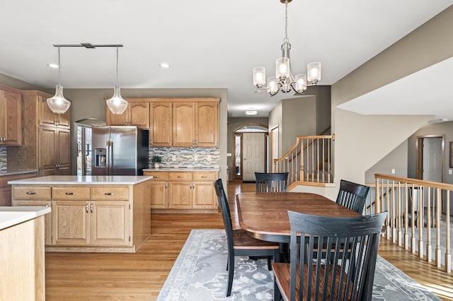 kitchen with light countertops, tasteful backsplash, stainless steel fridge with ice dispenser, and light wood-type flooring