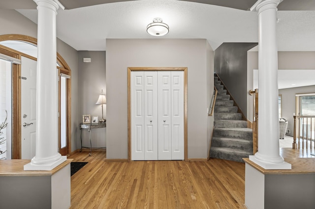 foyer featuring decorative columns, stairway, and light wood finished floors