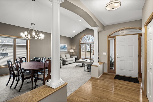 foyer featuring ornate columns, light wood-style floors, an inviting chandelier, baseboards, and vaulted ceiling