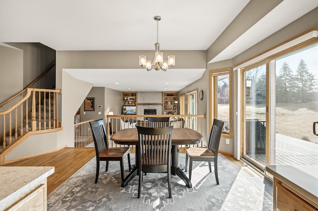 dining room featuring a notable chandelier, a fireplace, stairs, and light wood finished floors