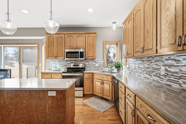 kitchen featuring light wood-style flooring, a sink, decorative backsplash, appliances with stainless steel finishes, and pendant lighting