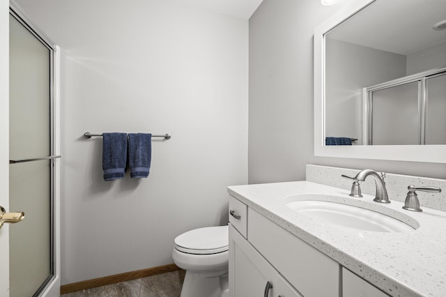 full bathroom featuring toilet, vanity, baseboards, and a shower with shower door