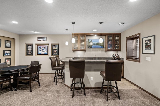 bar with indoor wet bar, hanging light fixtures, light colored carpet, and a textured ceiling