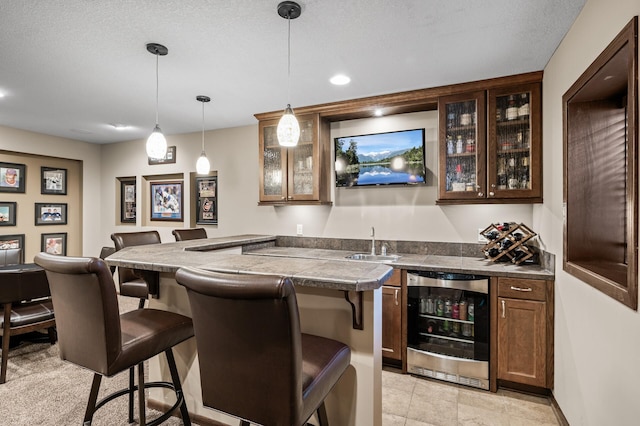 bar with beverage cooler, a sink, a textured ceiling, indoor wet bar, and hanging light fixtures