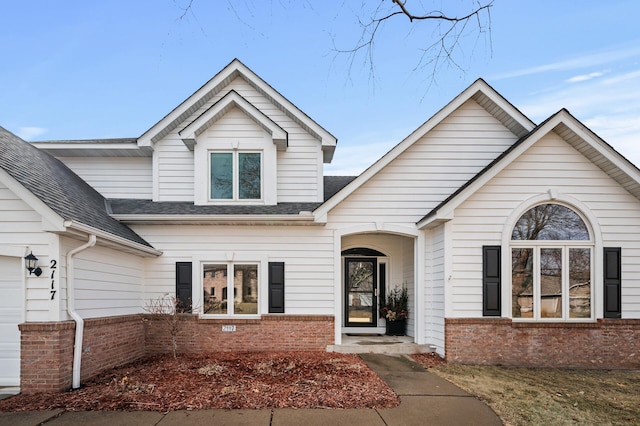 view of front of property featuring a garage, brick siding, and a shingled roof