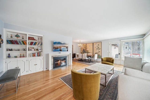 living room featuring light hardwood / wood-style floors, built in features, a premium fireplace, and an inviting chandelier