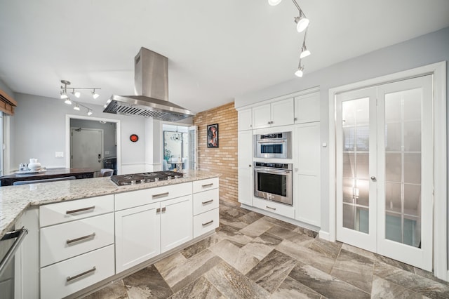 kitchen with white cabinets, island range hood, light stone countertops, and stainless steel appliances