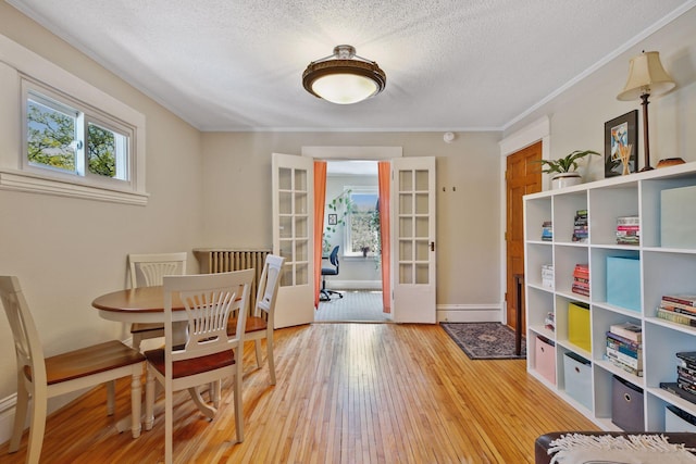 dining space with hardwood / wood-style flooring, crown molding, a textured ceiling, and french doors