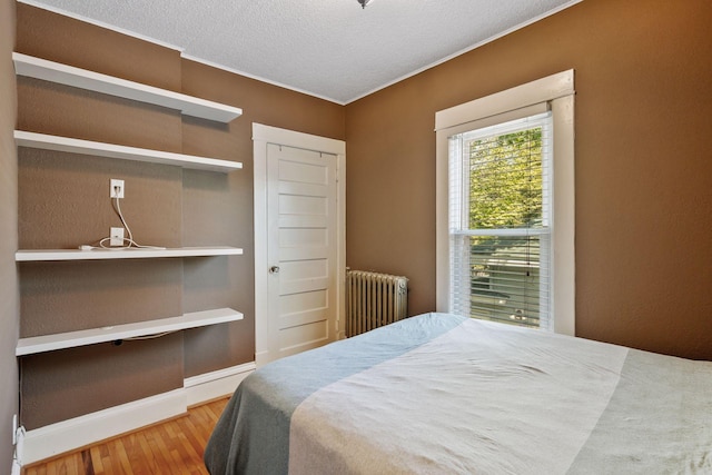 bedroom with radiator, a closet, wood-type flooring, and a textured ceiling