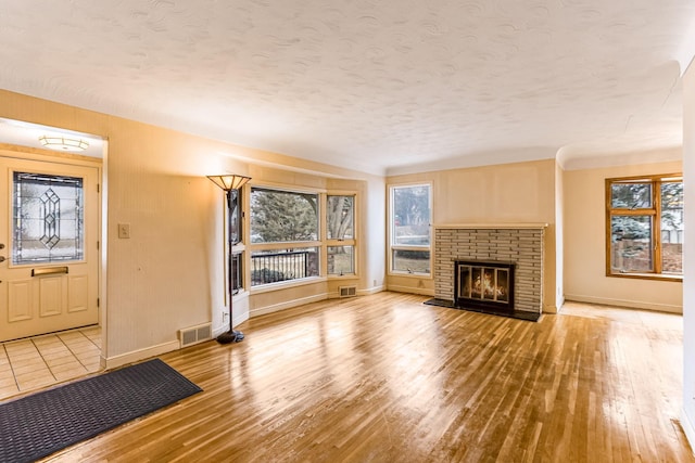 unfurnished living room featuring a fireplace, a textured ceiling, and light hardwood / wood-style floors