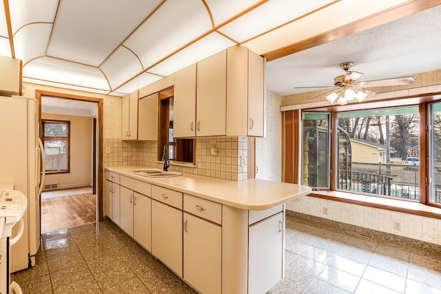 kitchen with kitchen peninsula, tasteful backsplash, ceiling fan, sink, and white refrigerator