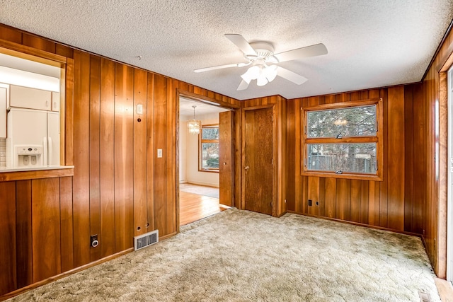 carpeted empty room featuring ceiling fan with notable chandelier, plenty of natural light, and wooden walls