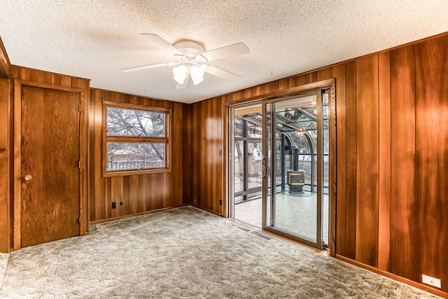 carpeted spare room with ceiling fan, wood walls, and a textured ceiling