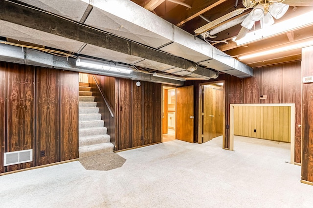 basement featuring light colored carpet, ceiling fan, and wood walls